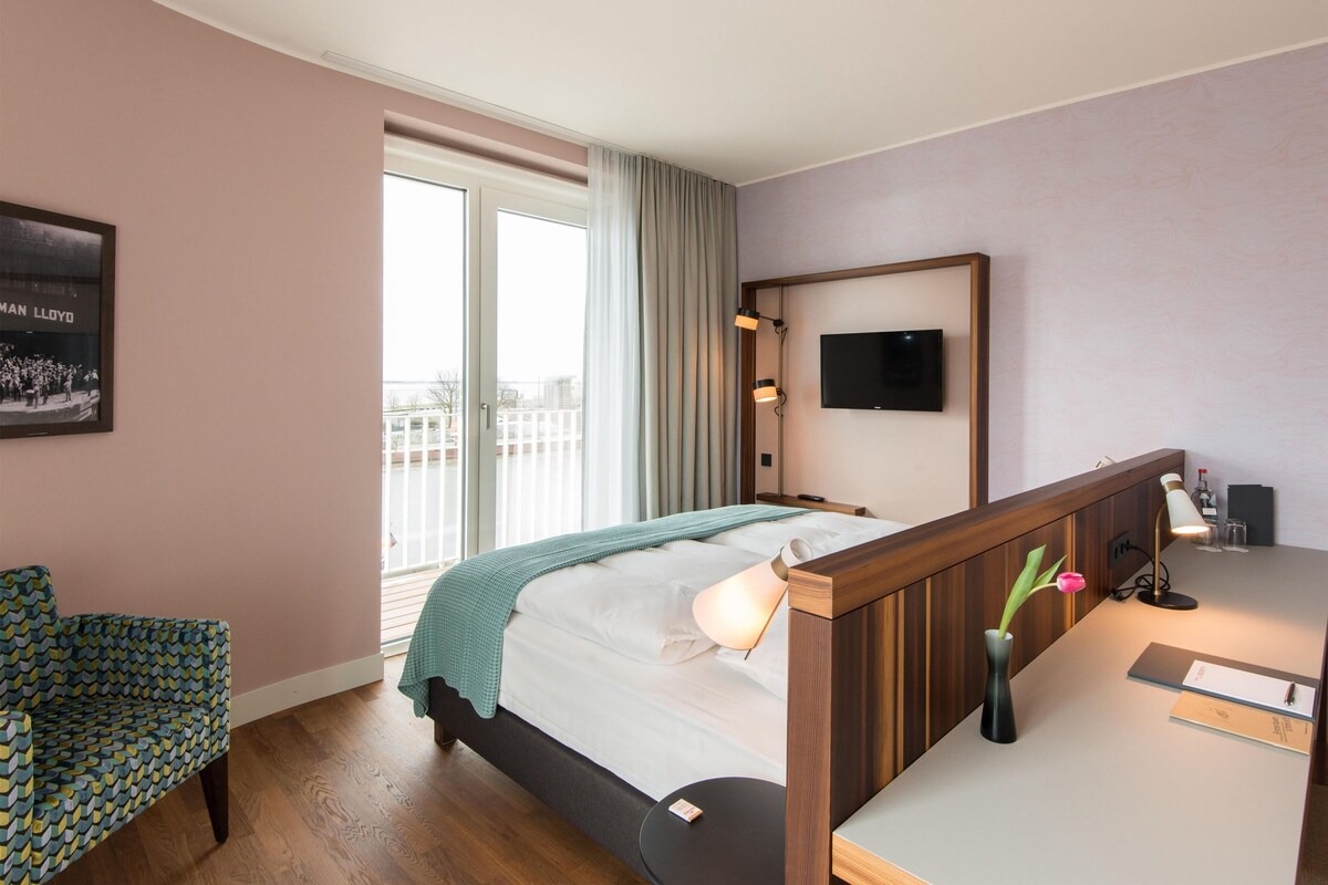 A hotel room with a bed, a desk, a chair, a television, and a balcony with a view.
