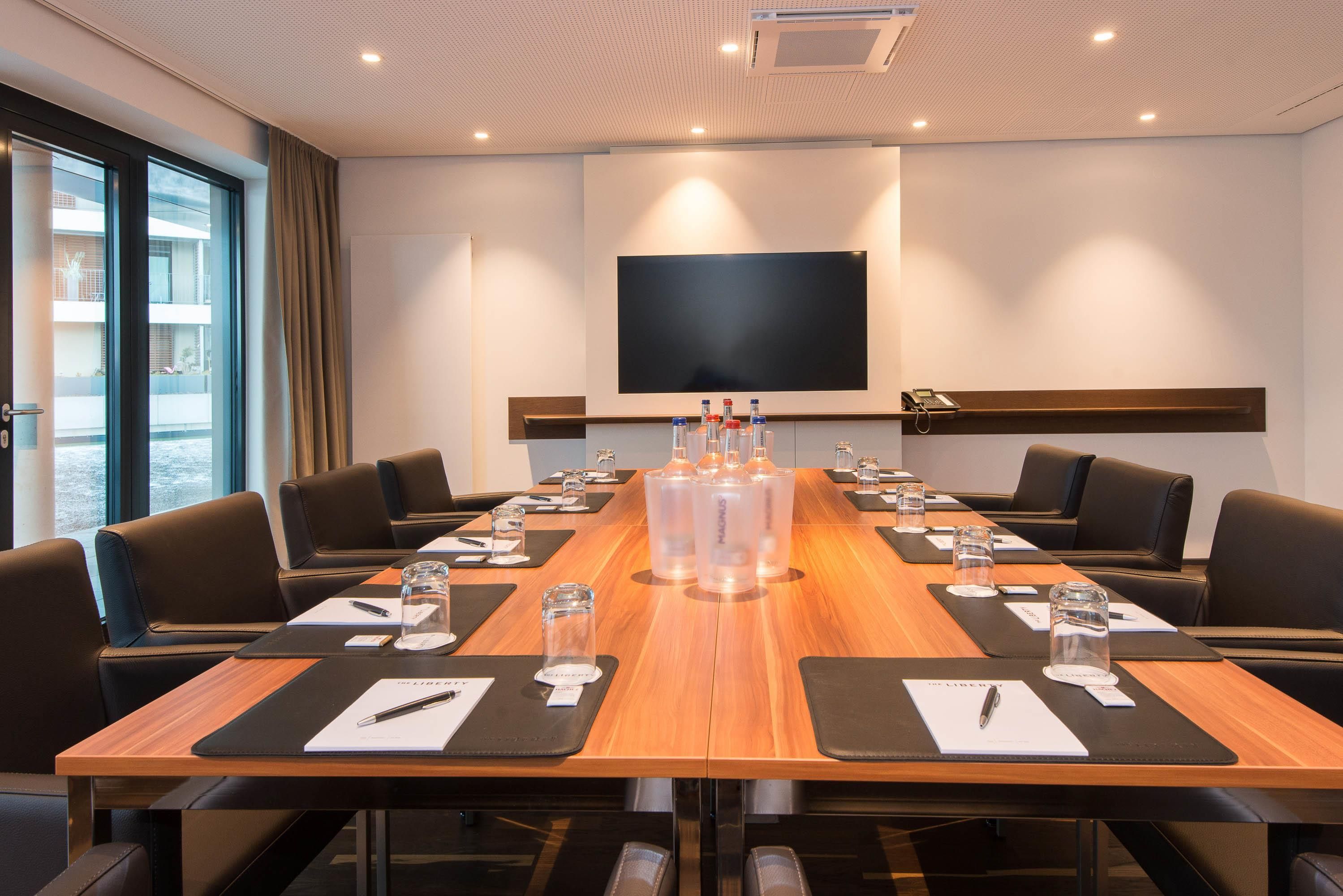 A conference room with a long table, black leather chairs, and a flat-screen TV mounted on the wall.