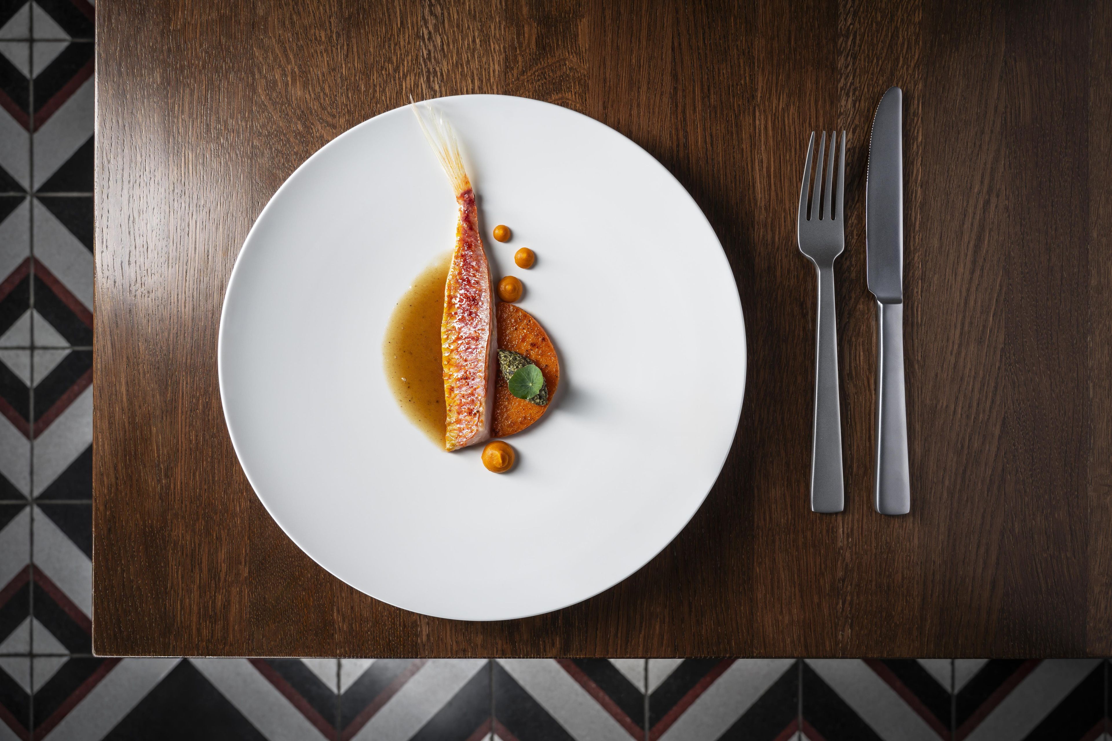 Une assiette blanche contenant un poisson, une sauce et une garniture, le tout posé sur une table en bois.