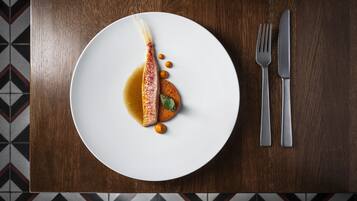 Une assiette blanche contenant un poisson, une sauce et une garniture, le tout posé sur une table en bois.