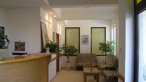 Zona de recepción con un escritorio de madera, un sofá, una mesa de centro y dos plantas en macetas.