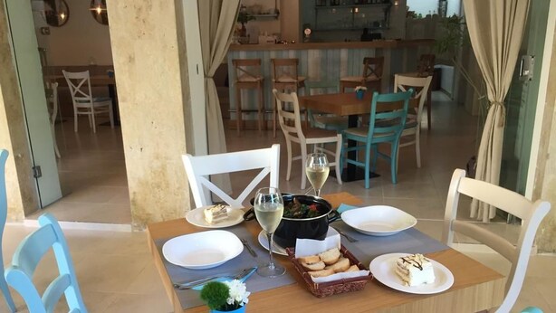 Un comedor con una mesa de madera dispuesta para dos personas, un tazón de sopa, un plato de pan y una copa de vino blanco.