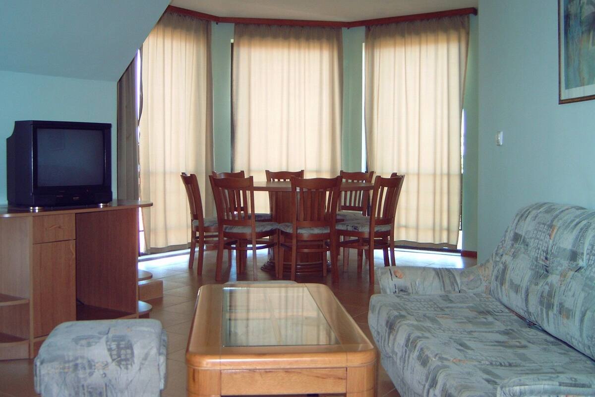 Un salon comprenant un téléviseur, une table à manger en bois, des chaises, un canapé et une table basse avec un plateau en verre.