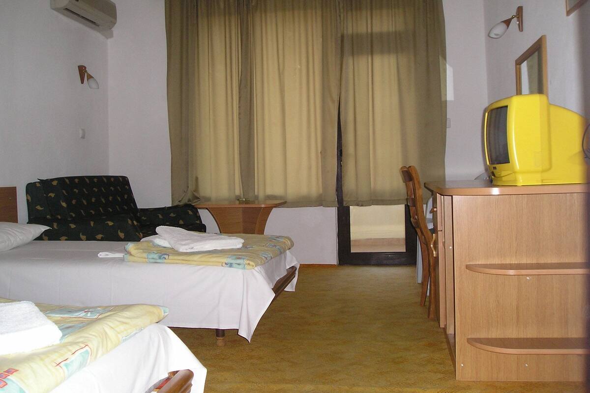 Une chambre d’hôtel avec deux lits, un bureau, une chaise, une télévision et une fenêtre avec des rideaux.