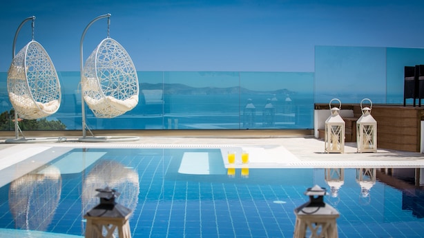 A pool with hanging chairs and lanterns, a clear view of the sea, and a wooden deck. - Villa Artemis, Wine Dark Sea Villas (Malevizi)