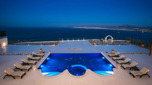 Piscina infinita com espreguiçadeiras e vista para o oceano ao entardecer.