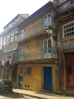 A multi-story building with balconies, a car parked in front, and a cobblestone street. - Casa Sao Miguel 6 (Porto)