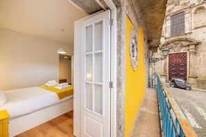A room with a bed, a door, a yellow wall, and a street view. - Casa Sao Miguel 6 (Porto)