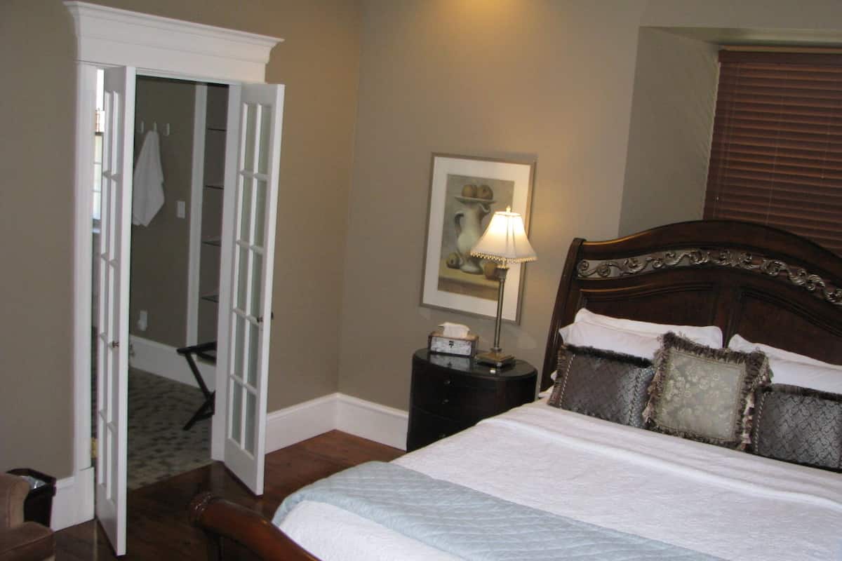 A neatly made bed with a wooden headboard, a bedside table with a lamp, and a framed picture on the wall.