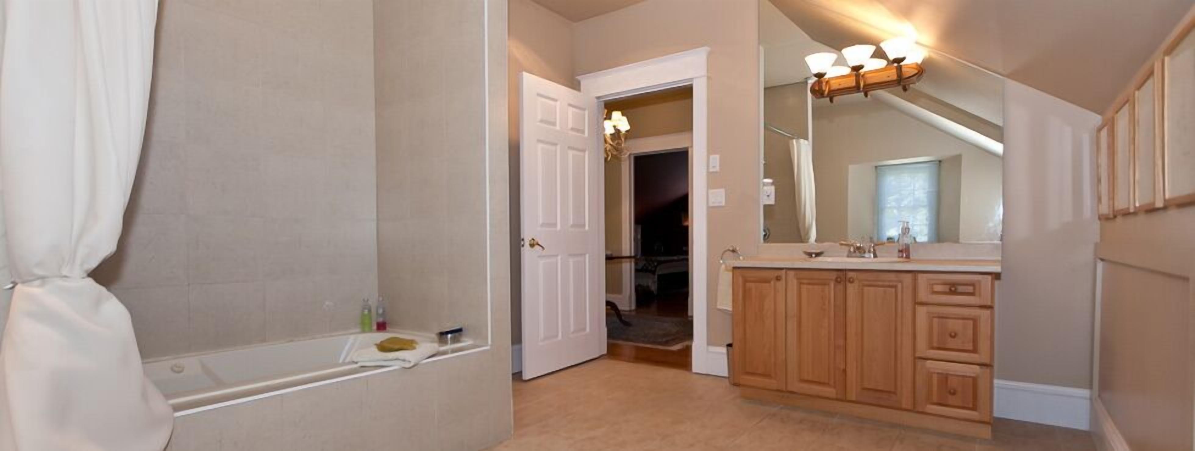 Un baño con bañera, tocador con espejo y puerta que da a otra habitación.
