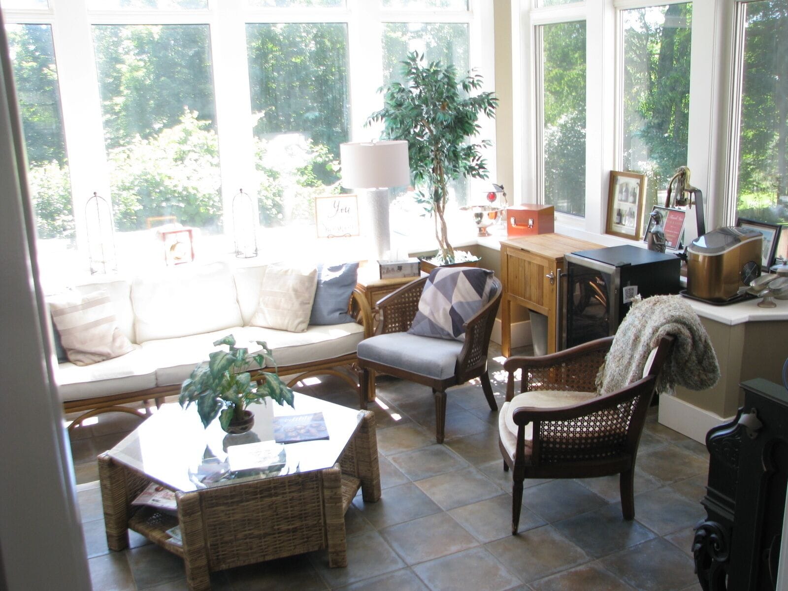 A sunlit living room with a sofa, chairs, a table, and a view of greenery outside.