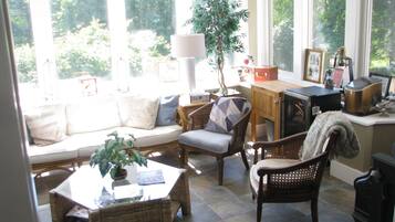 A sunlit living room with a sofa, chairs, a table, and a view of greenery outside.