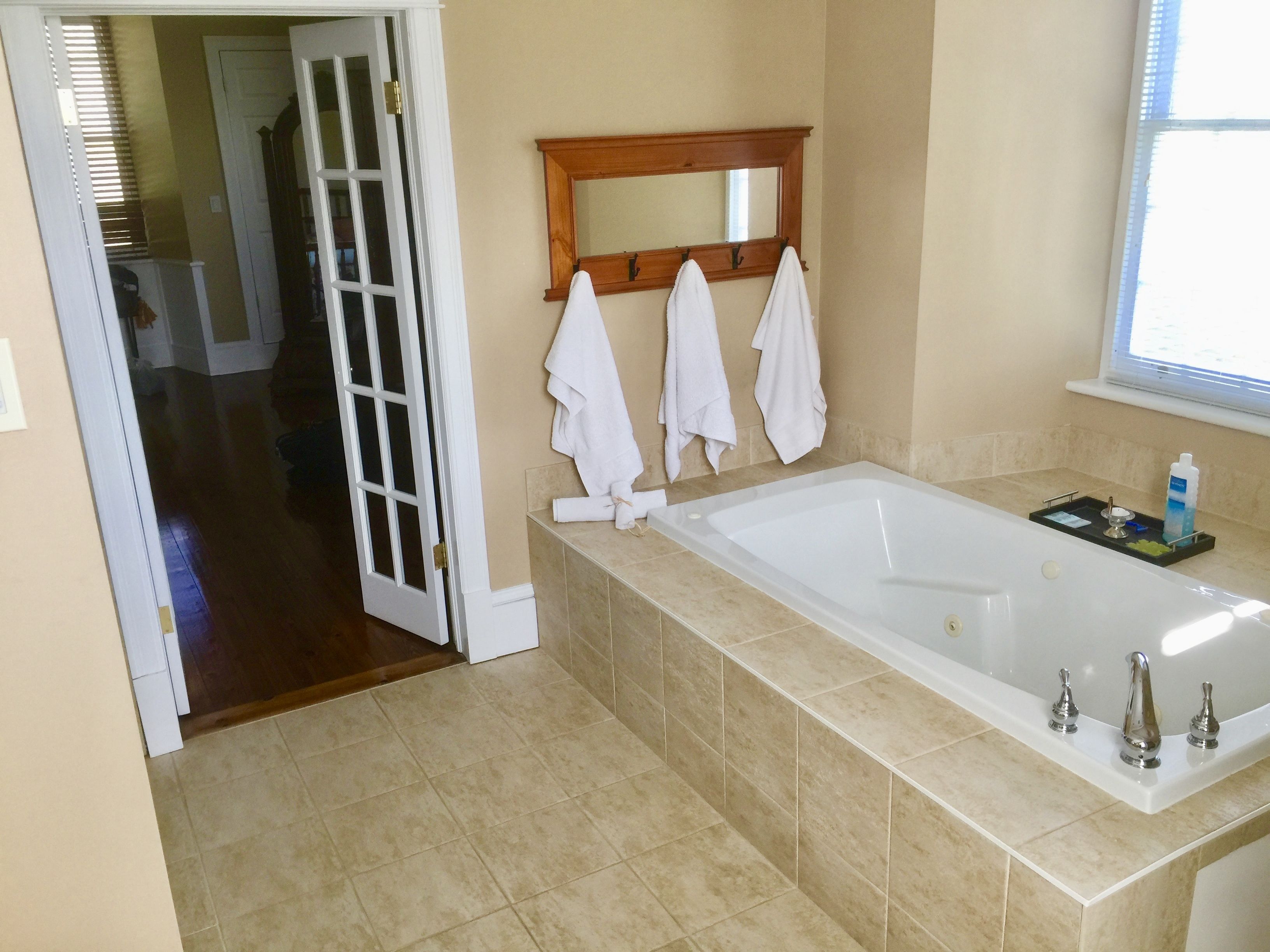 A bathroom with a large bathtub, a wooden-framed mirror, and three white towels hanging on hooks.