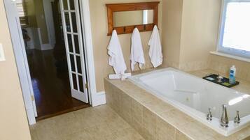 A bathroom with a large bathtub, a wooden-framed mirror, and three white towels hanging on hooks.