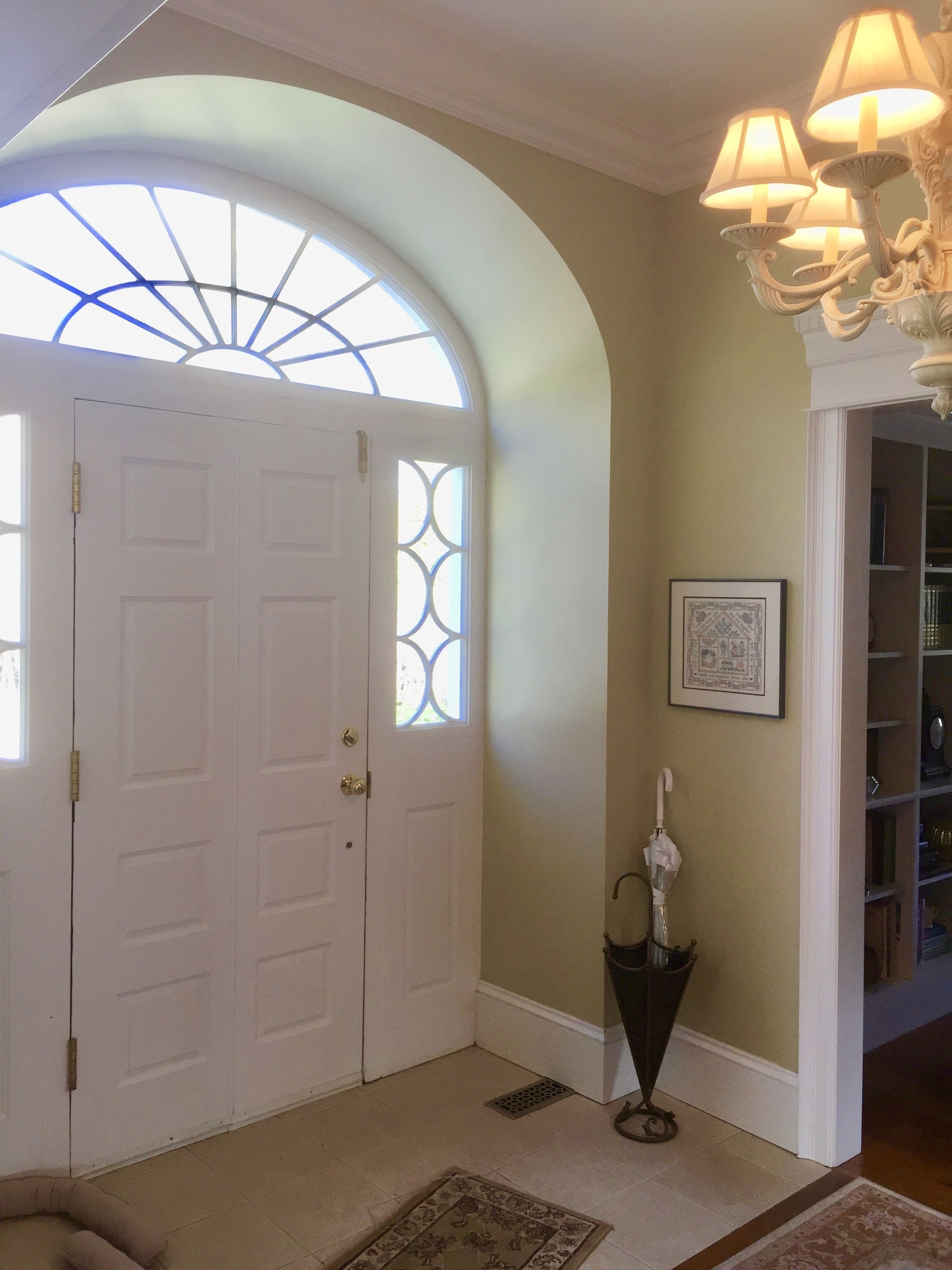 Ein Korridor mit einer weißen Tür, einem Fenster mit dekorativem Glasmuster, einem gerahmten Bild an der Wand und einem schwarzen Regenschirm, der an der Wand angelehnt ist.