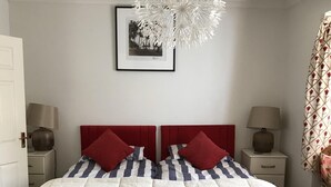 A bedroom with a bed, two bedside tables, a wall-mounted picture, and a ceiling light fixture. - Gwynarth B&B (Wadebridge)