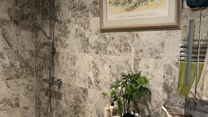 A modern bathroom with a glass-enclosed shower, a sink with a white countertop, and a framed picture of a beach scene. - Gwynarth B&B (Wadebridge)
