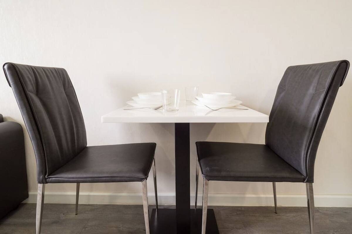 A dining area with two black leather chairs and a white table, featuring a glass and a few plates.