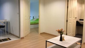 A modern, well-lit room with a white table, a small vase with flowers, and a view into another room with a bed and a window. - Chateau In Town By Renvio (Bangkok)