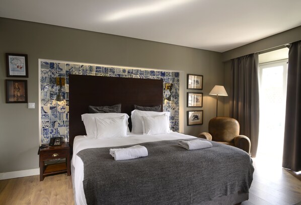 Habitación de hotel con una cama grande, una mesita de noche, una silla y una pared con azulejos azules y blancos.