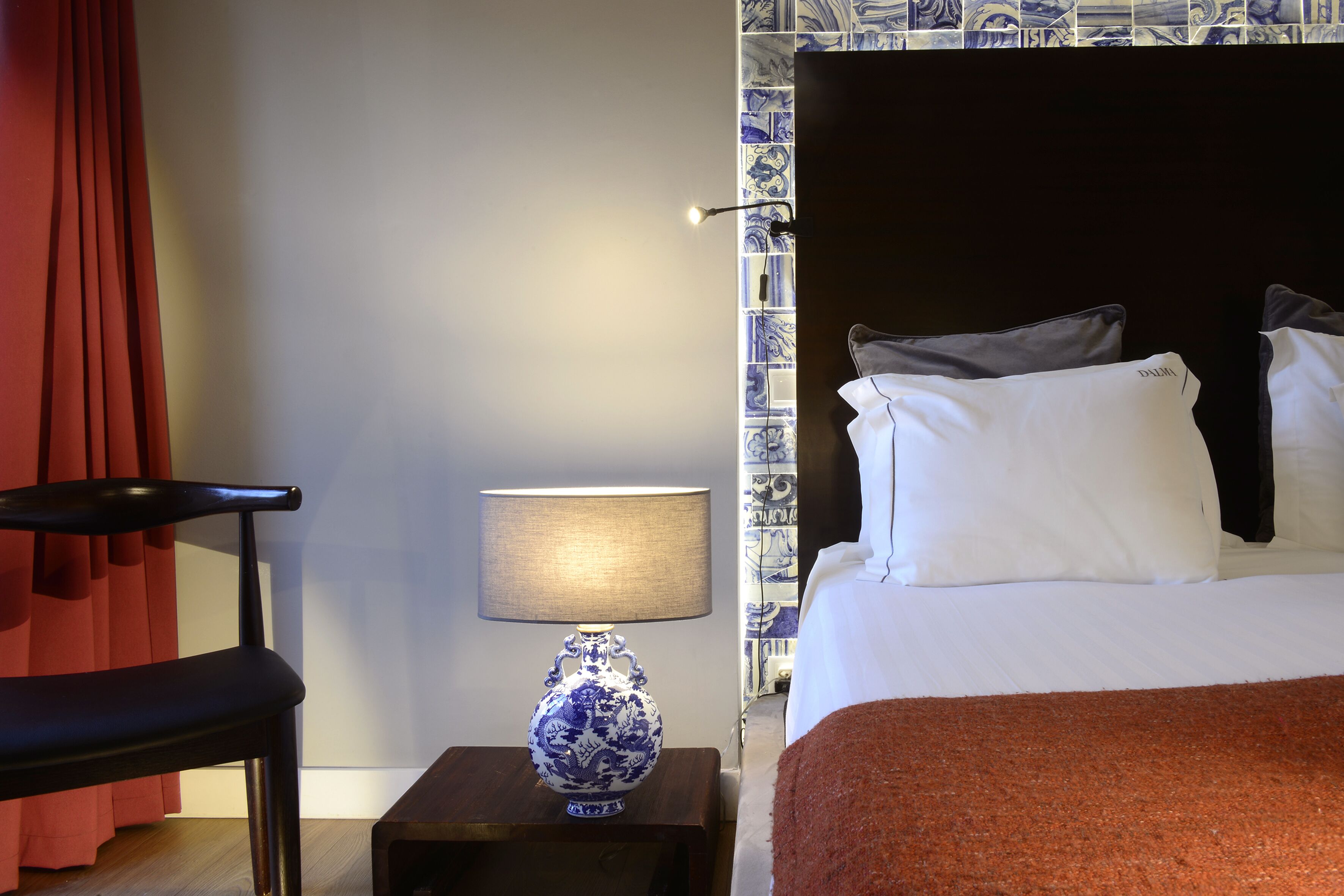 Una habitación de hotel con una cama, una mesita de noche con lámpara, una silla y un jarrón decorativo.