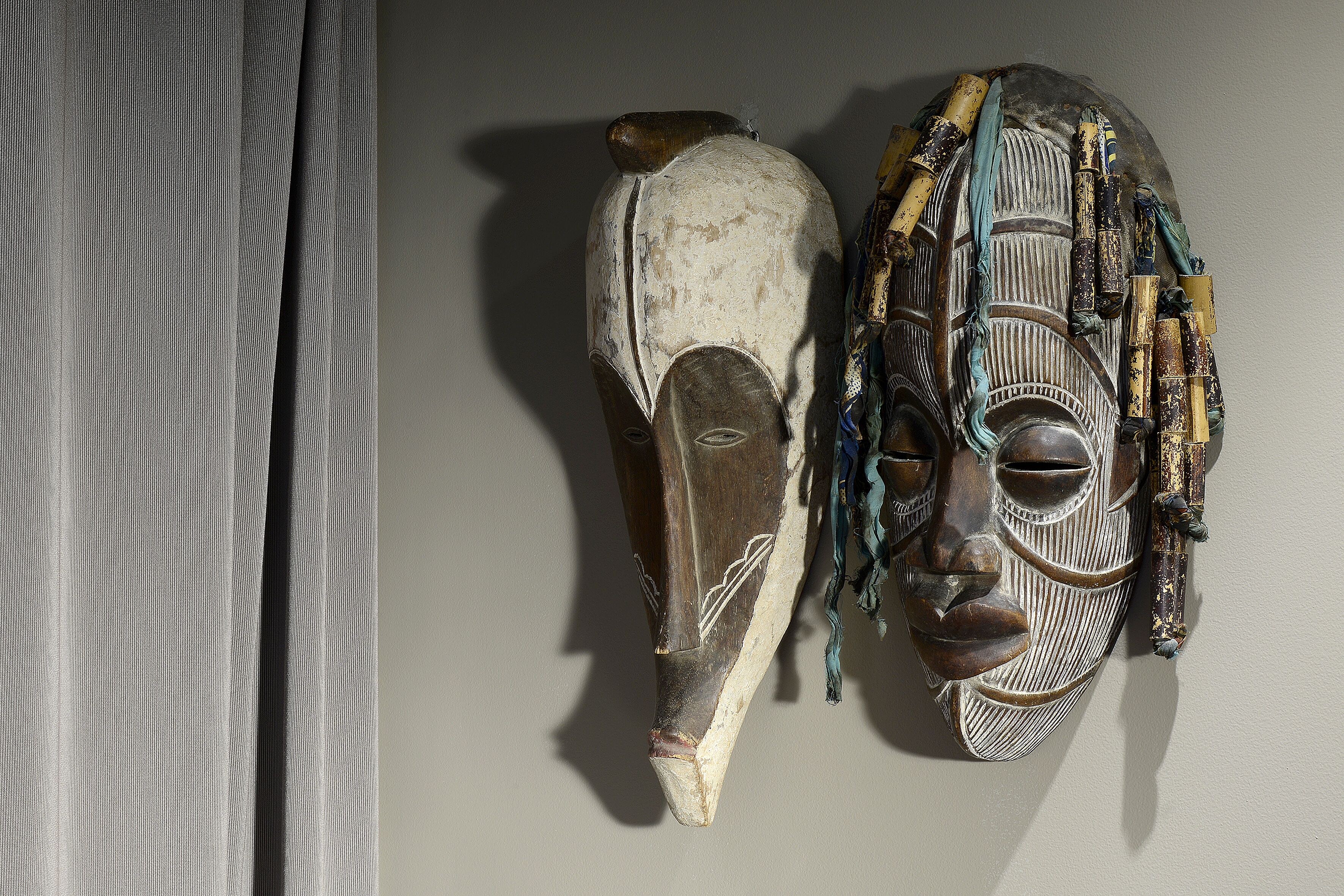 Two wooden masks with intricate carvings and beadwork, displayed against a plain wall.