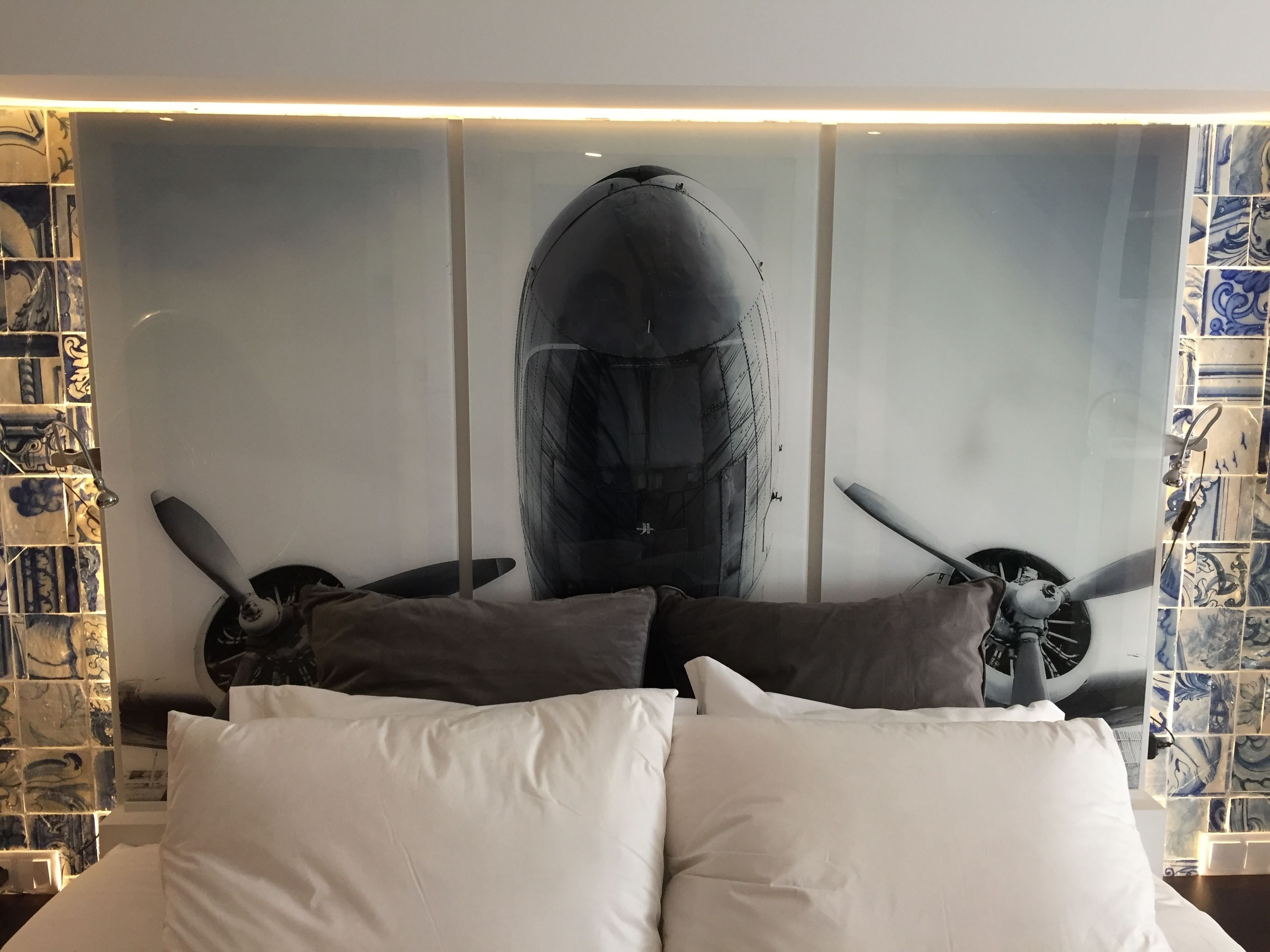 A bed with white pillows and a large abstract painting of a whale and propellers on the wall behind it.