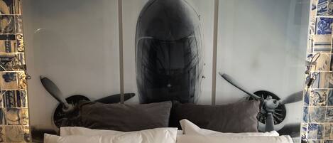 A bed with white pillows and a large abstract painting of a whale and propellers on the wall behind it.