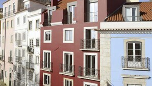 Uma fileira de edifícios altos com varandas, uma rua de calçada e um céu azul e claro.