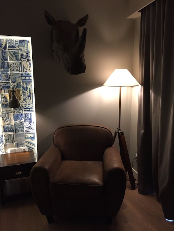 A room with a brown leather chair, a lamp, a wall-mounted animal head, and a tiled wall.