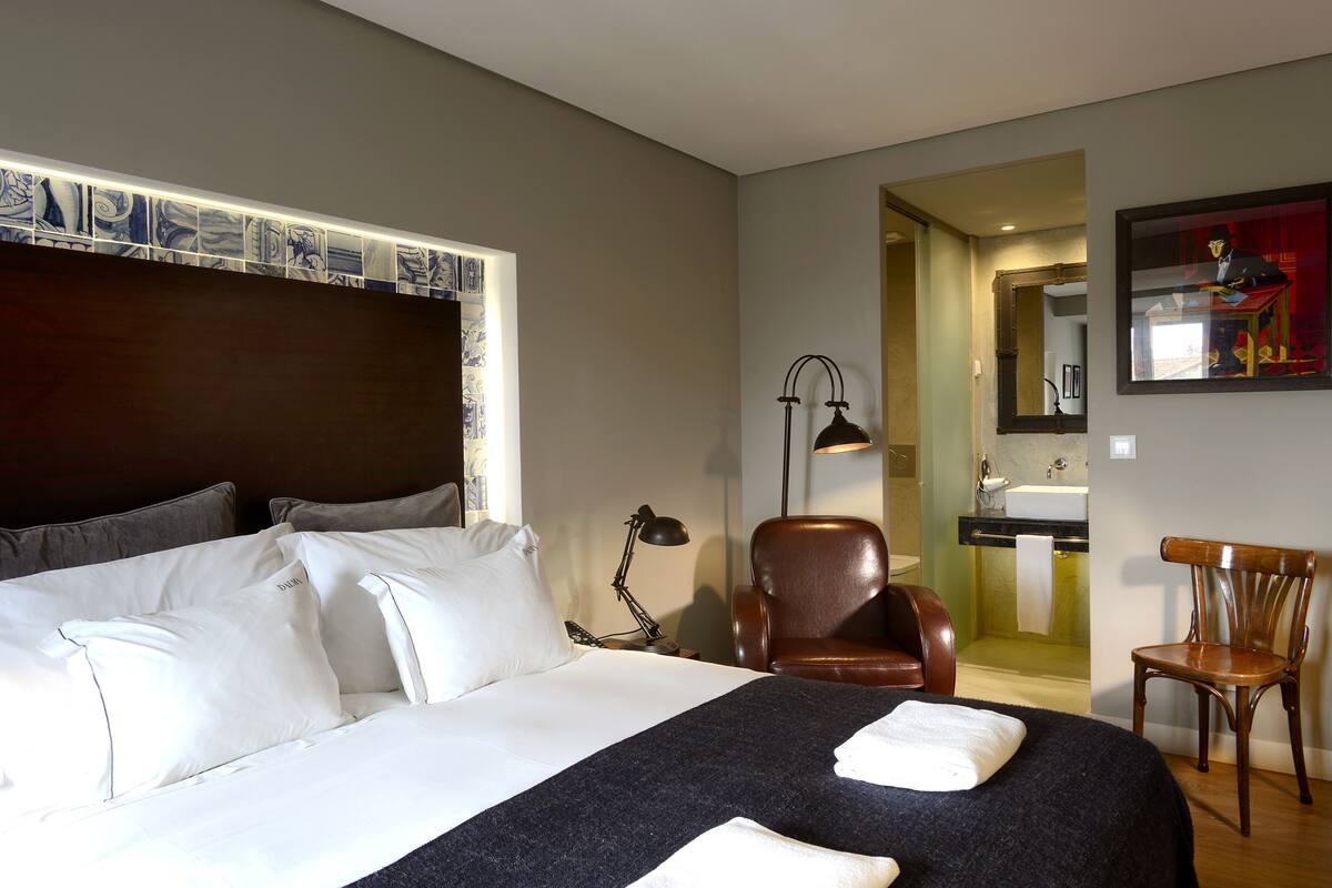 Une chambre d’hôtel avec un grand lit, un bureau, une chaise, une lampe et une salle de bain visible à travers une porte ouverte.