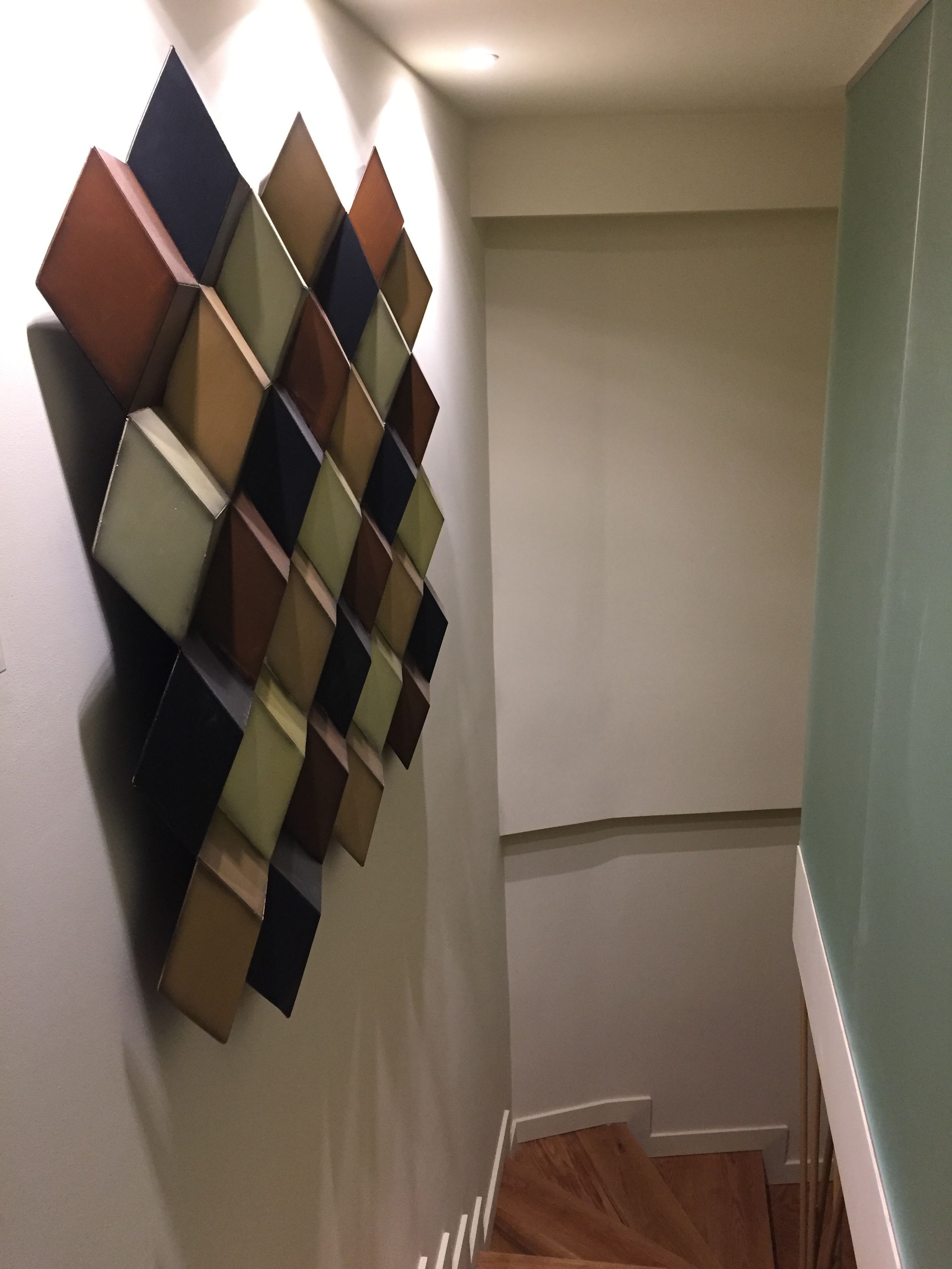 A corner of a room with a wall-mounted geometric art piece and a staircase.