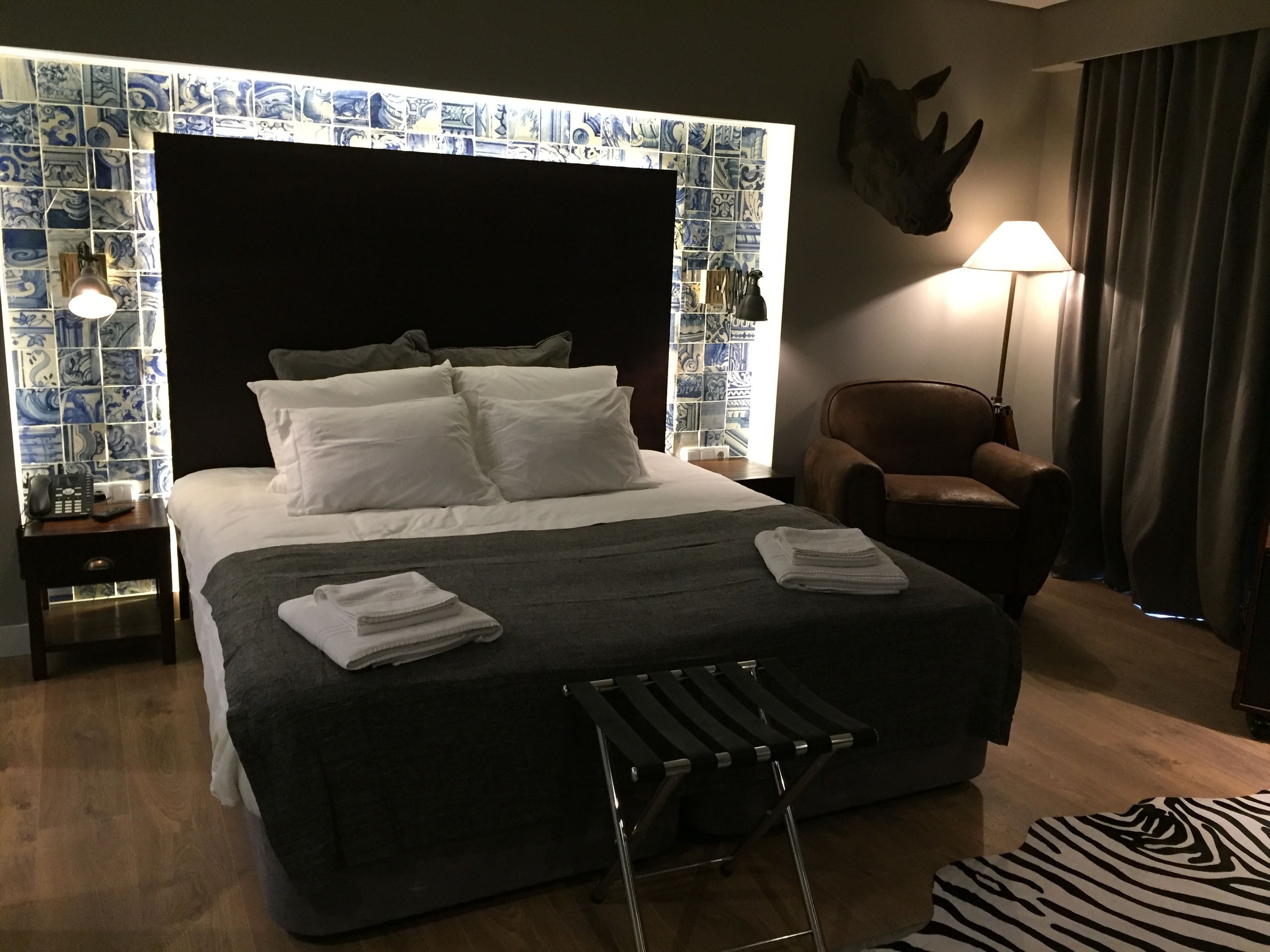 Cama bem arrumada com lençóis brancos, cabeceira preta e tapete com padrão de zebra.