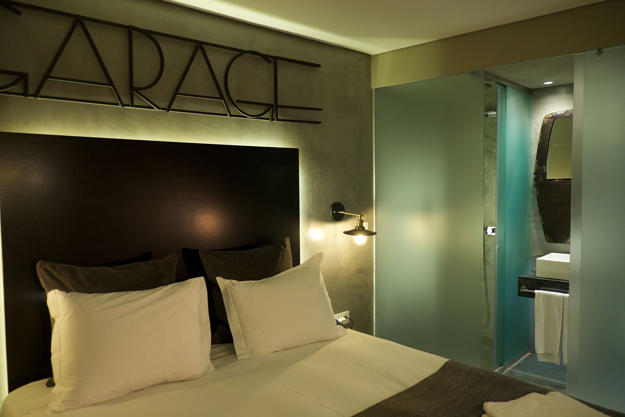 A hotel room with a bed, a wall-mounted light, and a door leading to a bathroom.