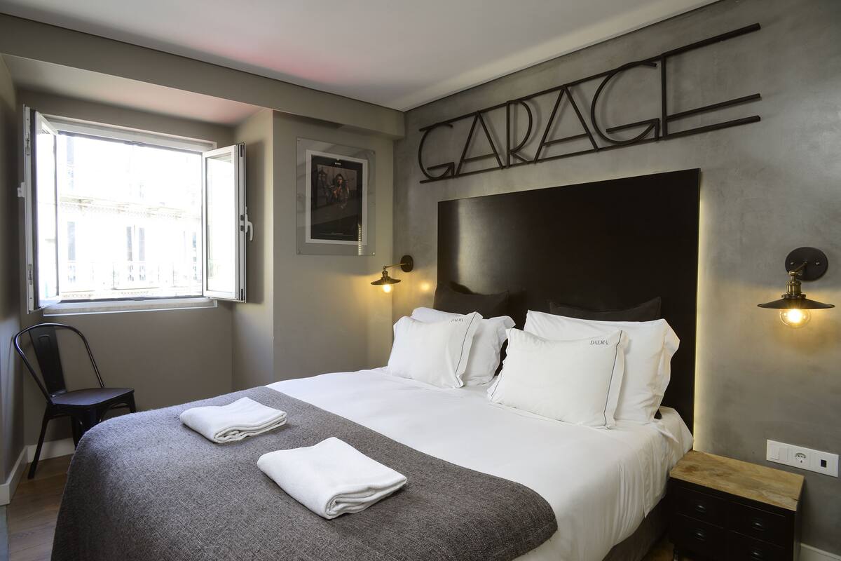 Une chambre d’hôtel avec un grand lit, une chaise, un bureau et une fenêtre donnant sur des immeubles.