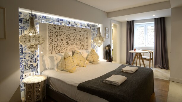 Quarto de hotel moderno com uma cama grande, azulejos decorativos na parede e duas luminárias pendentes.