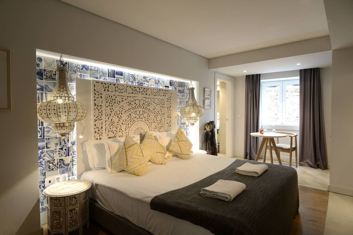 Une chambre d’hôtel moderne avec un grand lit, des carreaux décoratifs sur les murs et deux lampes suspendues.