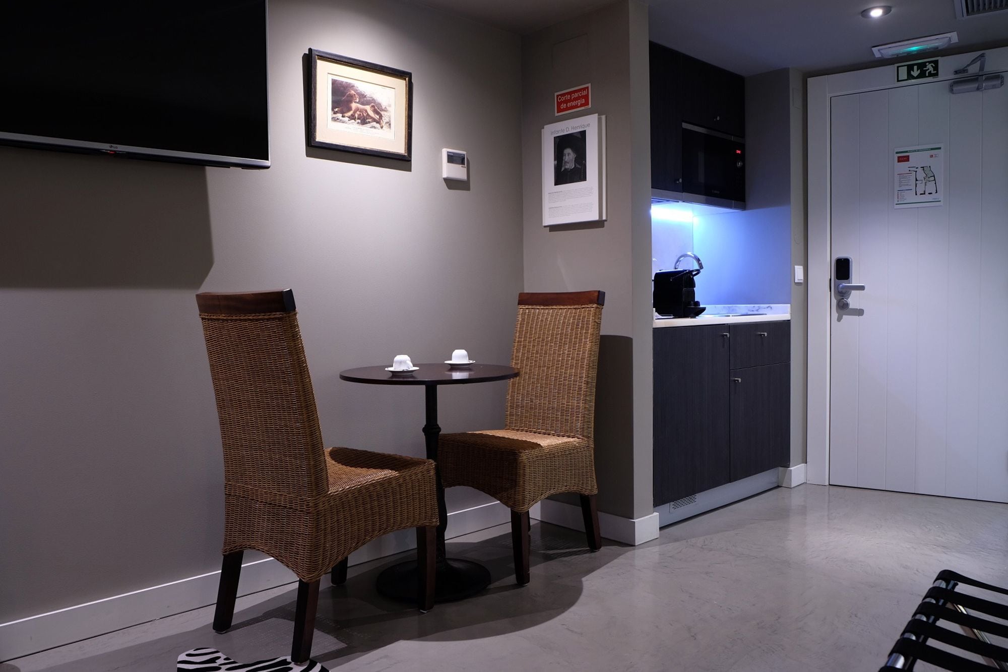 A small, modern room with two wicker chairs, a round table, a microwave, and a door with a sign.