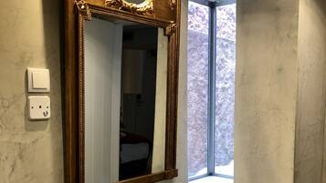 A bathroom with a marble wall, a white sink, a gold-framed mirror, and a window with a view of trees.