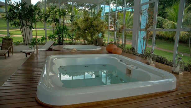 A hot tub on a wooden deck with lounge chairs and potted plants.