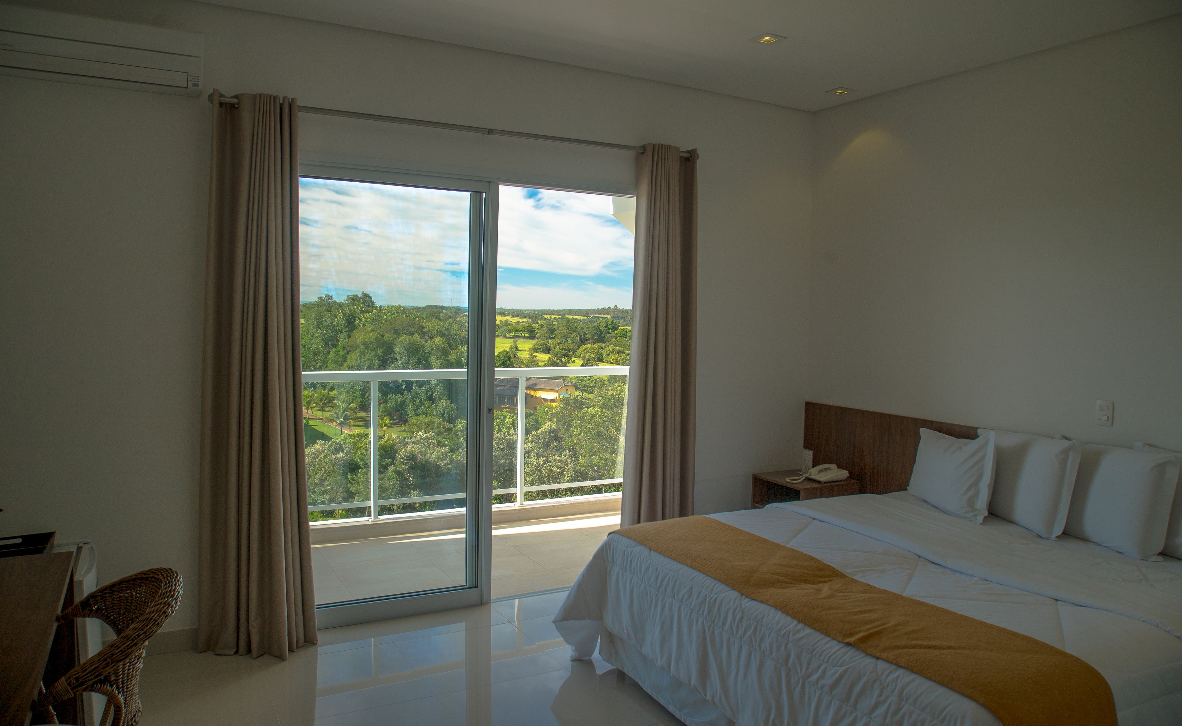 A modern bedroom with a large bed, a nightstand, a telephone, and a view of a green landscape through a sliding glass door.