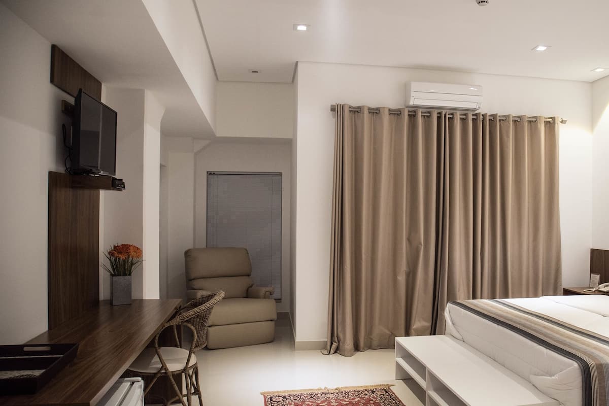 A modern bedroom with a bed, a desk, a chair, and a TV.