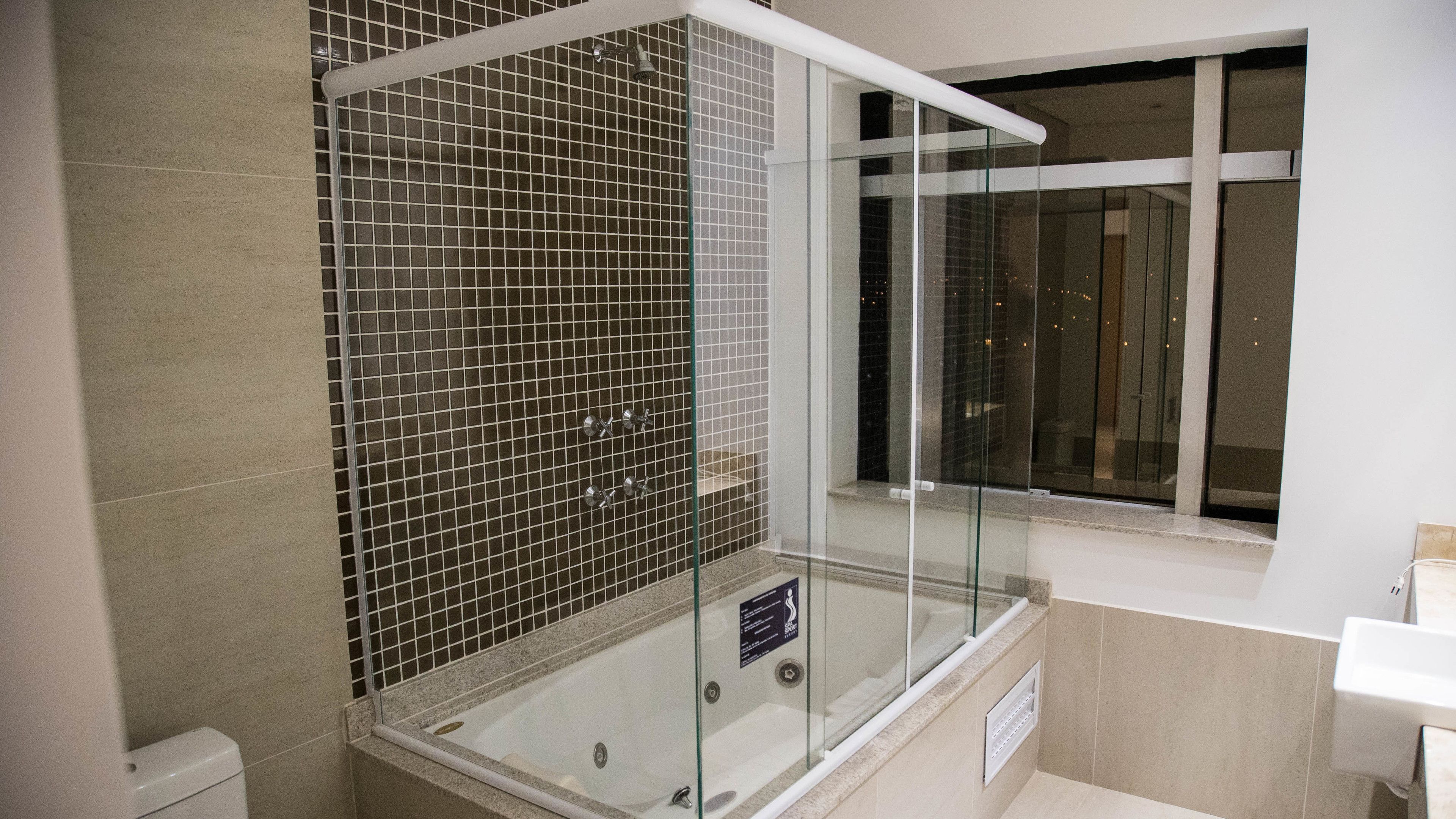 Un baño moderno con ducha envuelta en vidrio, una bañera y una ventana que ofrece vistas de la ciudad de noche.