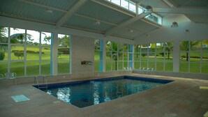 An indoor swimming pool with clear views of a golf course through large windows.