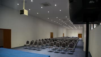 Uma sala de conferências com fileiras de cadeiras, uma mesa azul e um projetor.