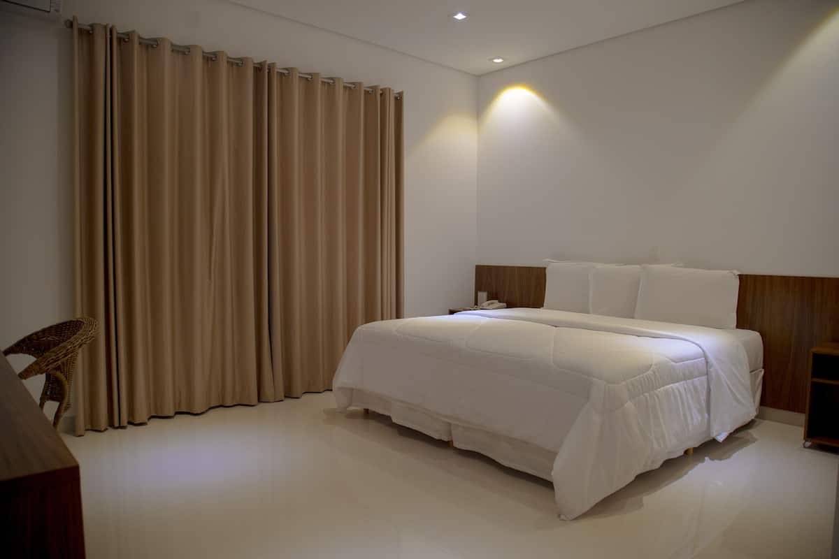 A bedroom with a large bed, a wooden headboard, a bedside table, and a chair.
