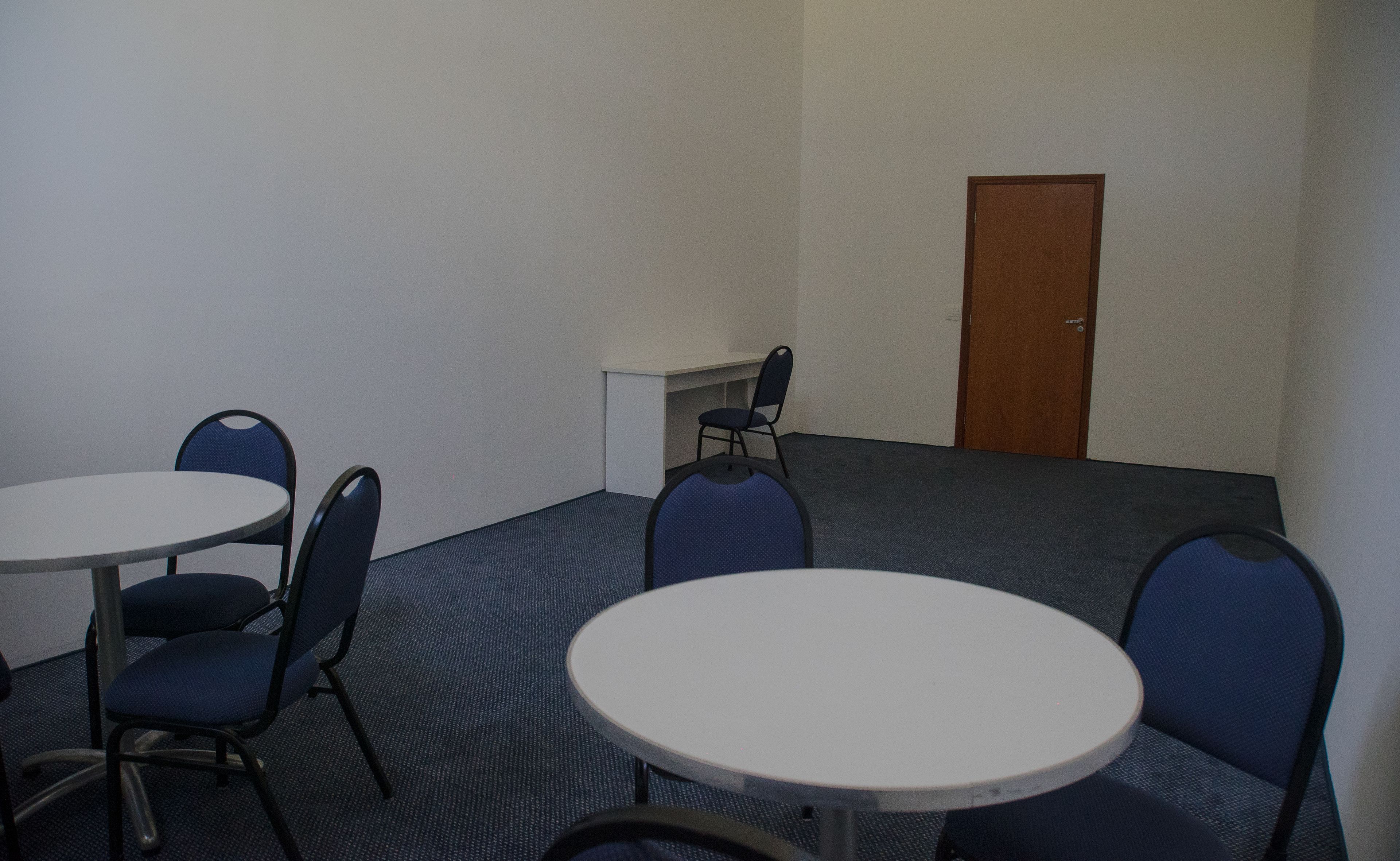 A room with a round table and four chairs, a small white desk, and a door.