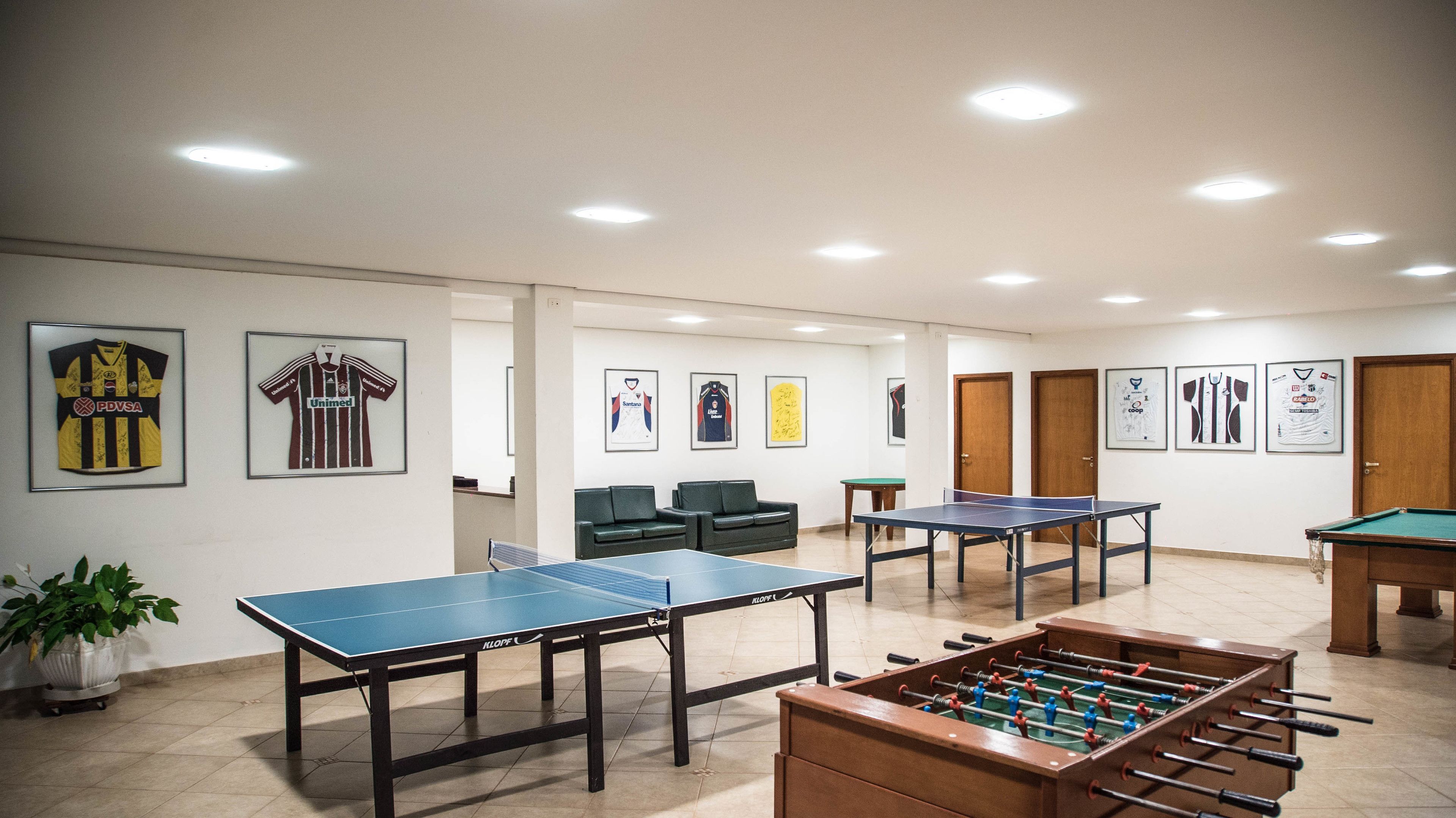A room with multiple ping pong tables, a foosball table, and sports jerseys on the wall.