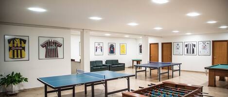 Una stanza con diversi tavoli da ping pong, un tavolo da calcio e maglie sportive appese alle pareti.