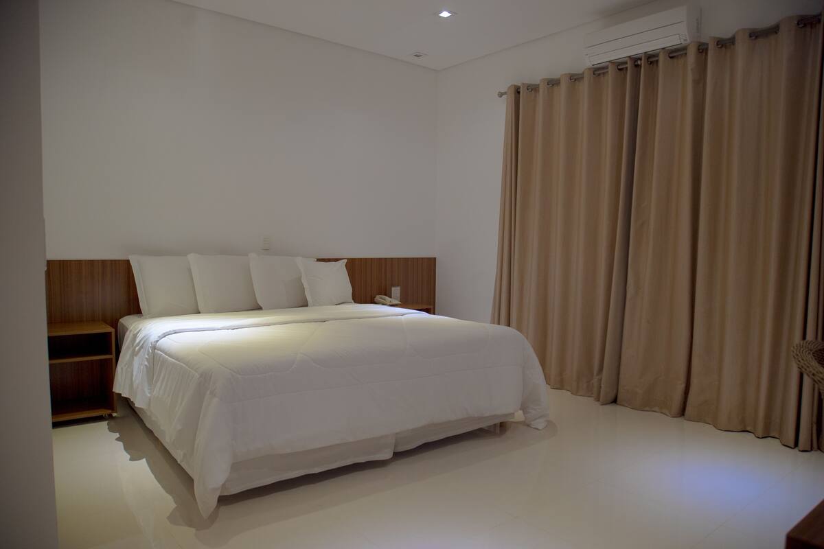 A bedroom with a large bed, a wooden headboard, a bedside table, and a curtain.